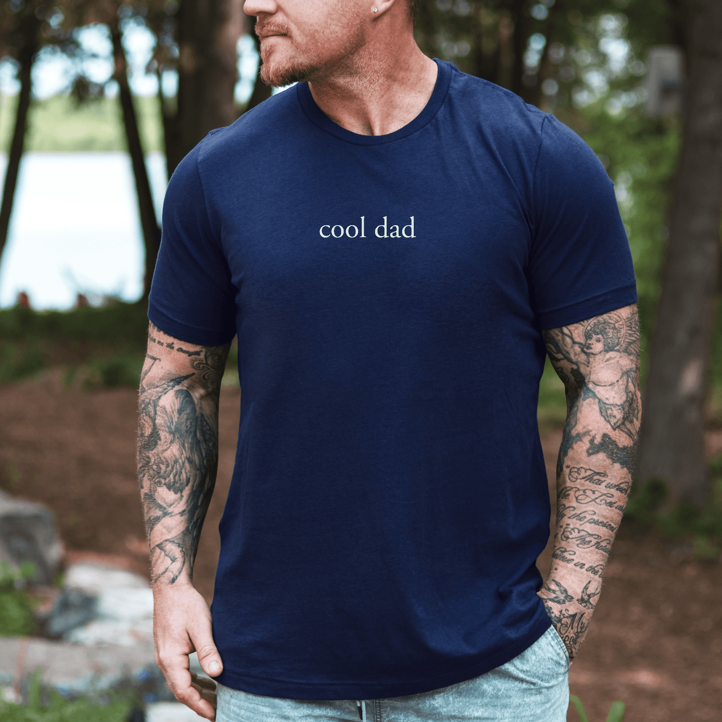 Minimalist Cool Dad Shirt navy t shirt with small cool dad text on chest worn by tattooed man outdoors casual dad gift