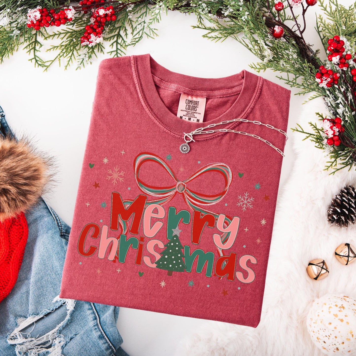 Preppy Merry Christmas Shirt folded red tee with bow and tree graphic styled with denim jacket and holiday greenery