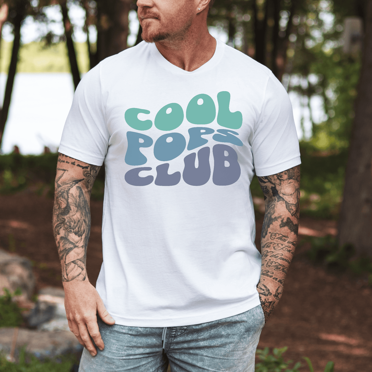 Man wearing Retro Cool Pops Club Shirt white tee with retro bubble print, tattoos, lakeside background