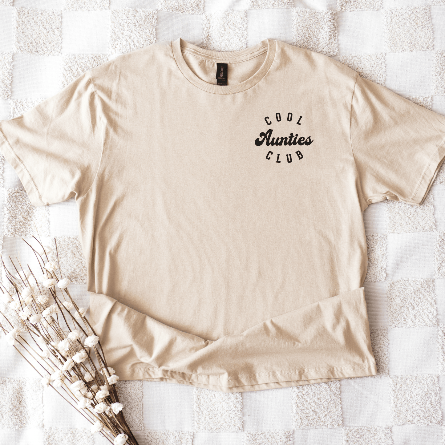 Maddy and George Designs beige cotton tee with small Cool Aunties Club Shirt chest logo on quilted blanket