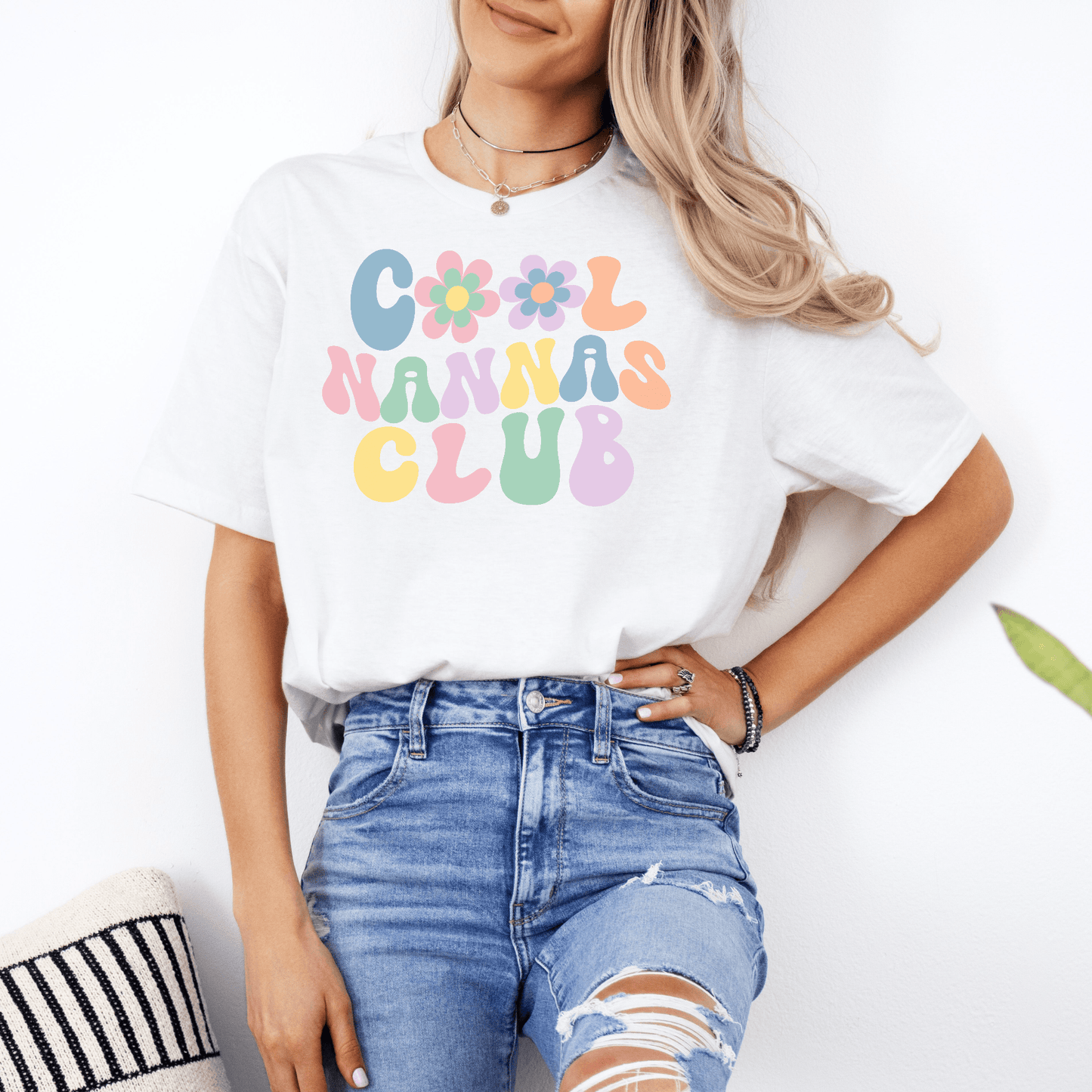 Woman wearing white Cool Nannas Club Shirt with pastel retro floral lettering and high waisted ripped jeans