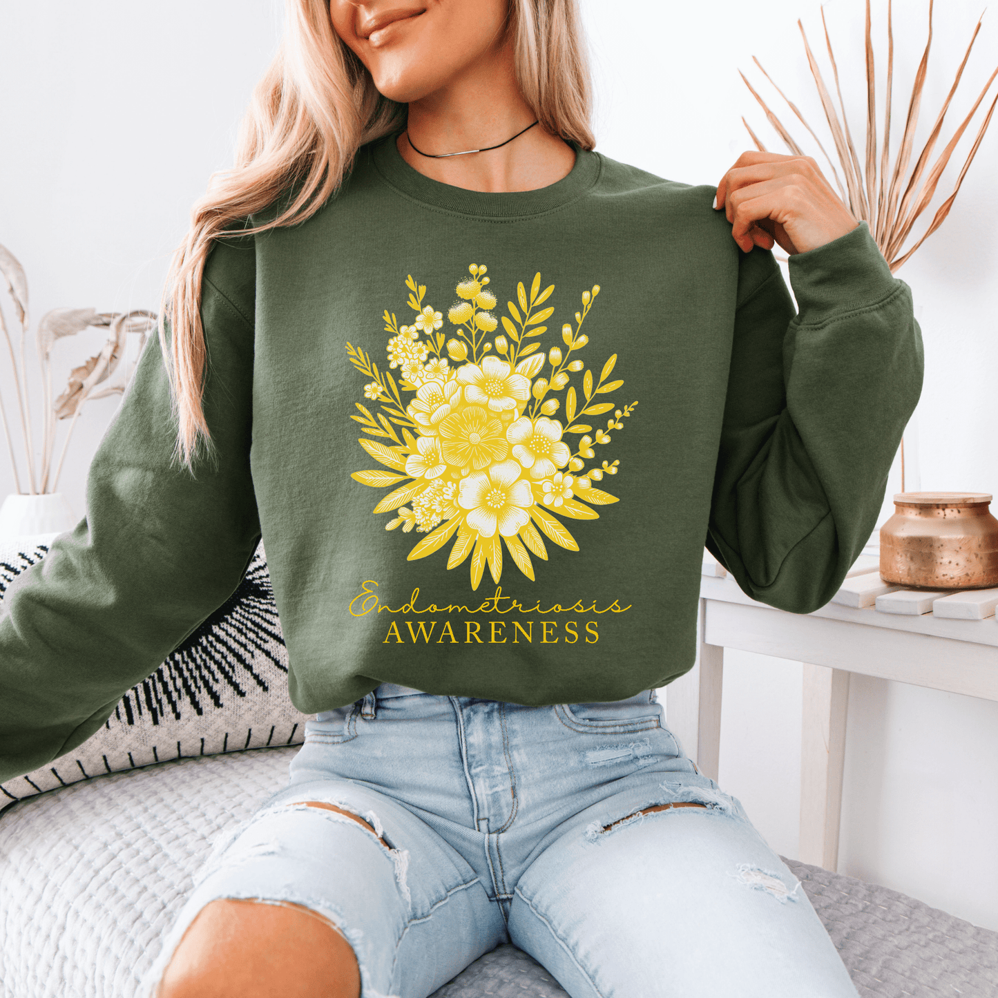 Woman wearing olive green Floral Endometriosis Awareness Sweatshirt . yellow floral bouquet print centered on chest seated pose