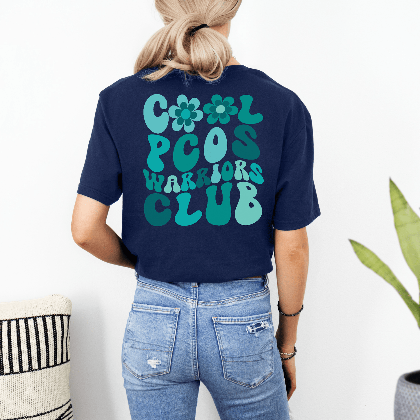 Back view of navy tee with teal retro floral Cool PCOS Warriors Club design worn by woman PCOS Awareness Shirt