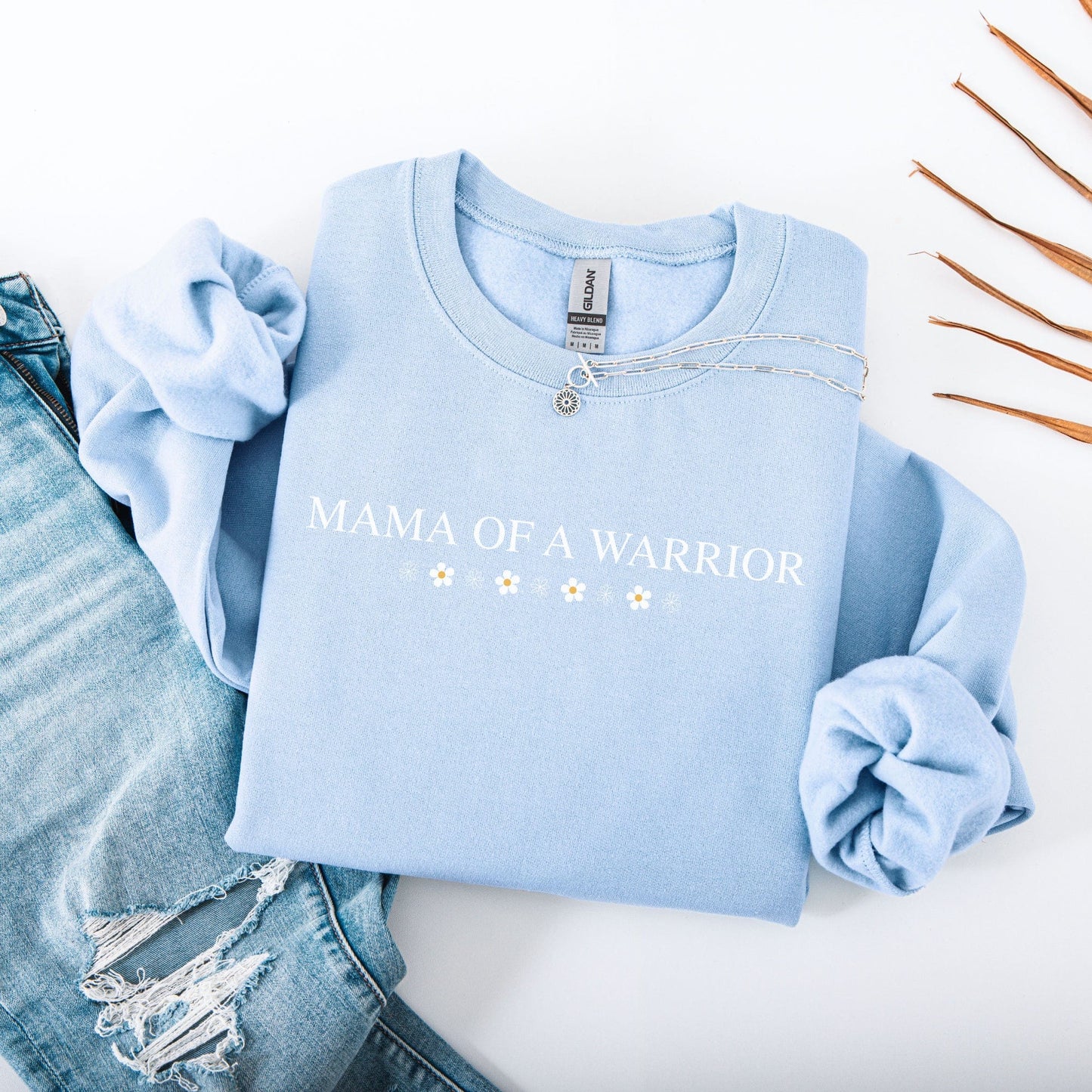 Mama of a Warrior Sweatshirt light blue crewneck with white lettering and daisy accents styled with jeans and necklace