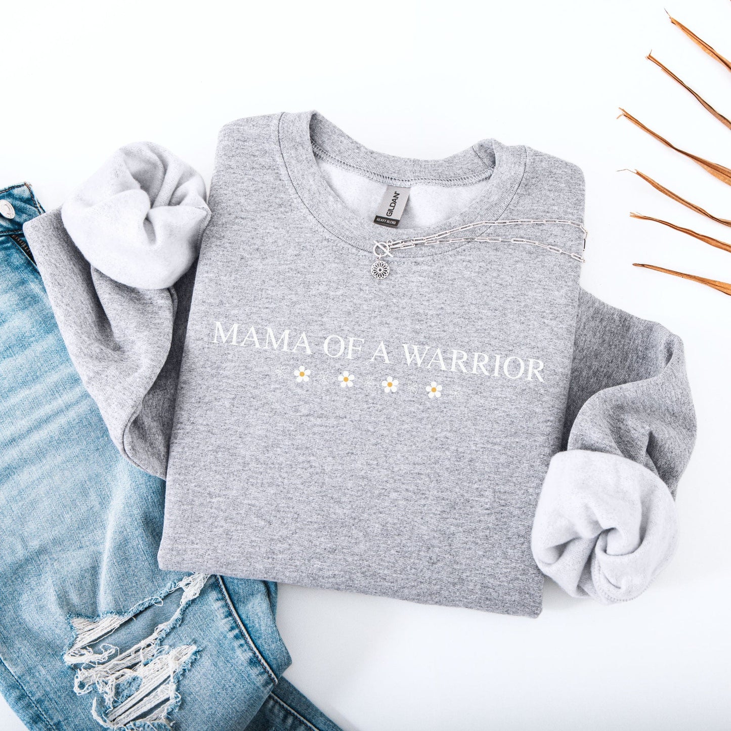 Grey Mama of a Warrior Sweatshirt folded with small daisy print styled with distressed jeans and necklace