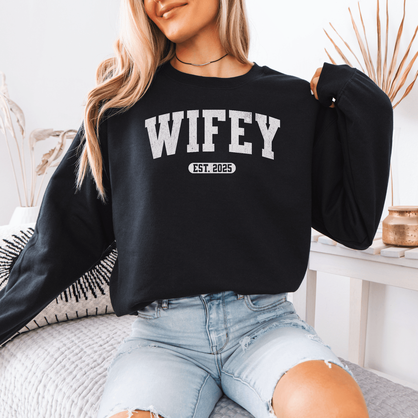 Model wearing black custom wifey sweatshirt with bold WIFEY print and EST 2025 paired with ripped light denim jeans