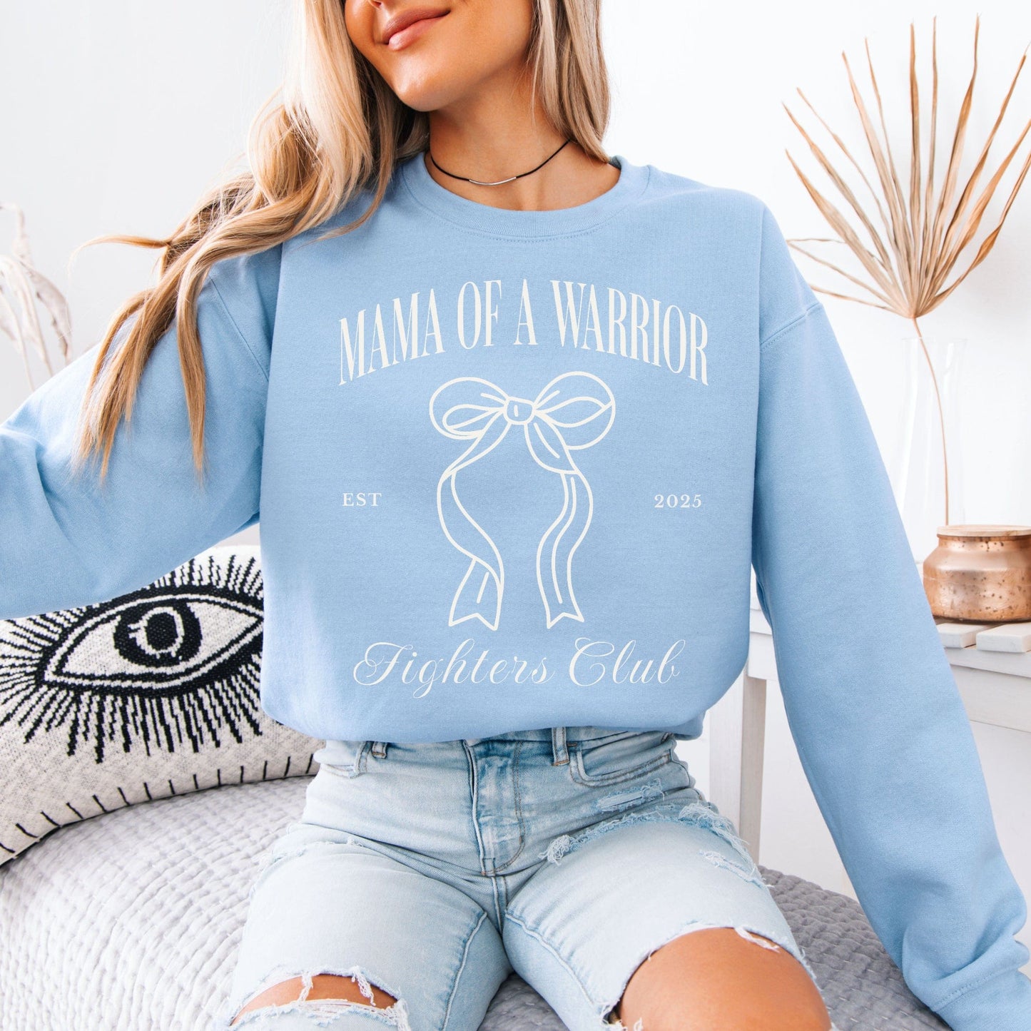 Medical Mom Gift light blue sweatshirt mockup reading Mama of a Warrior with bow design by Maddy and George Designs
