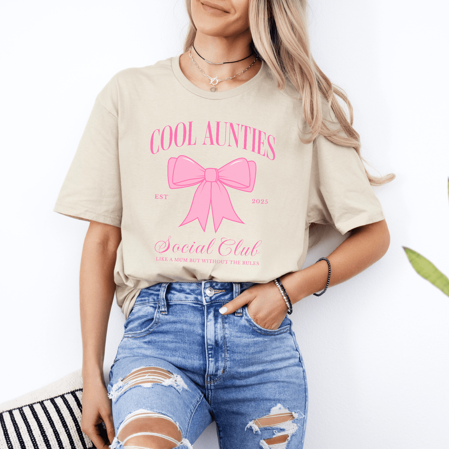 Model wearing Custom Cool Aunties Club Shirt beige tee with pink bow print and casual ripped jeans