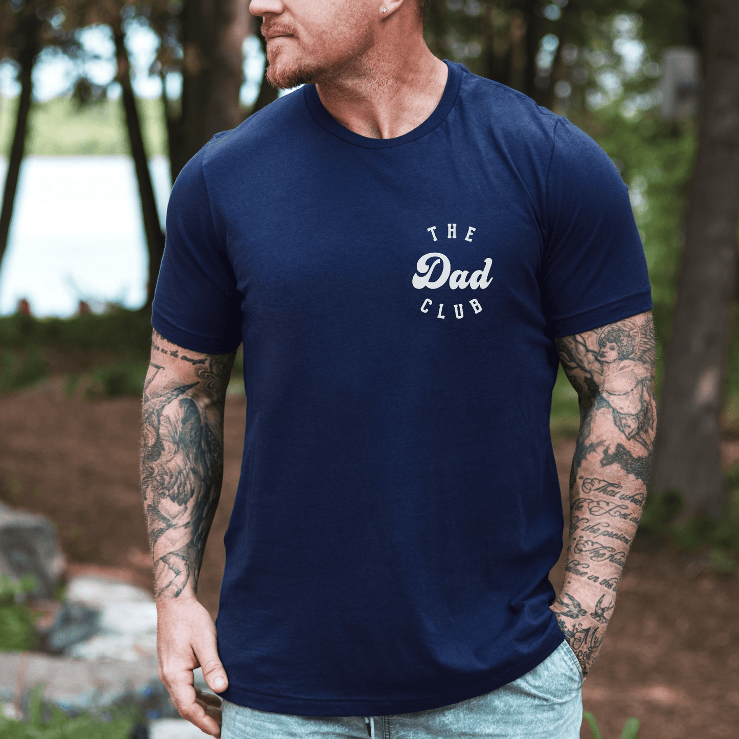 Man wearing navy Cool Dads Club Shirt with small white chest logo outdoors by lake