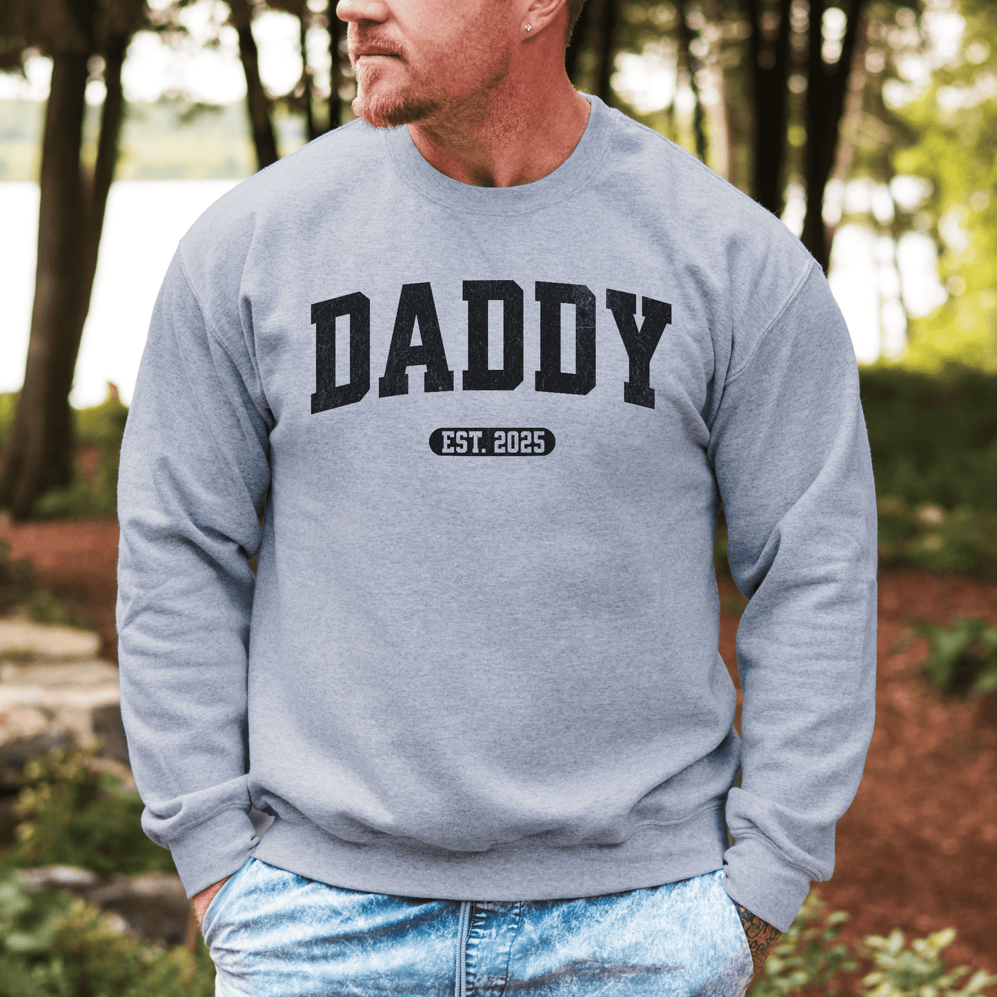 Man wearing gray crewneck Daddy Sweatshirt with Custom Year printed DADDY and EST 2025 outdoors