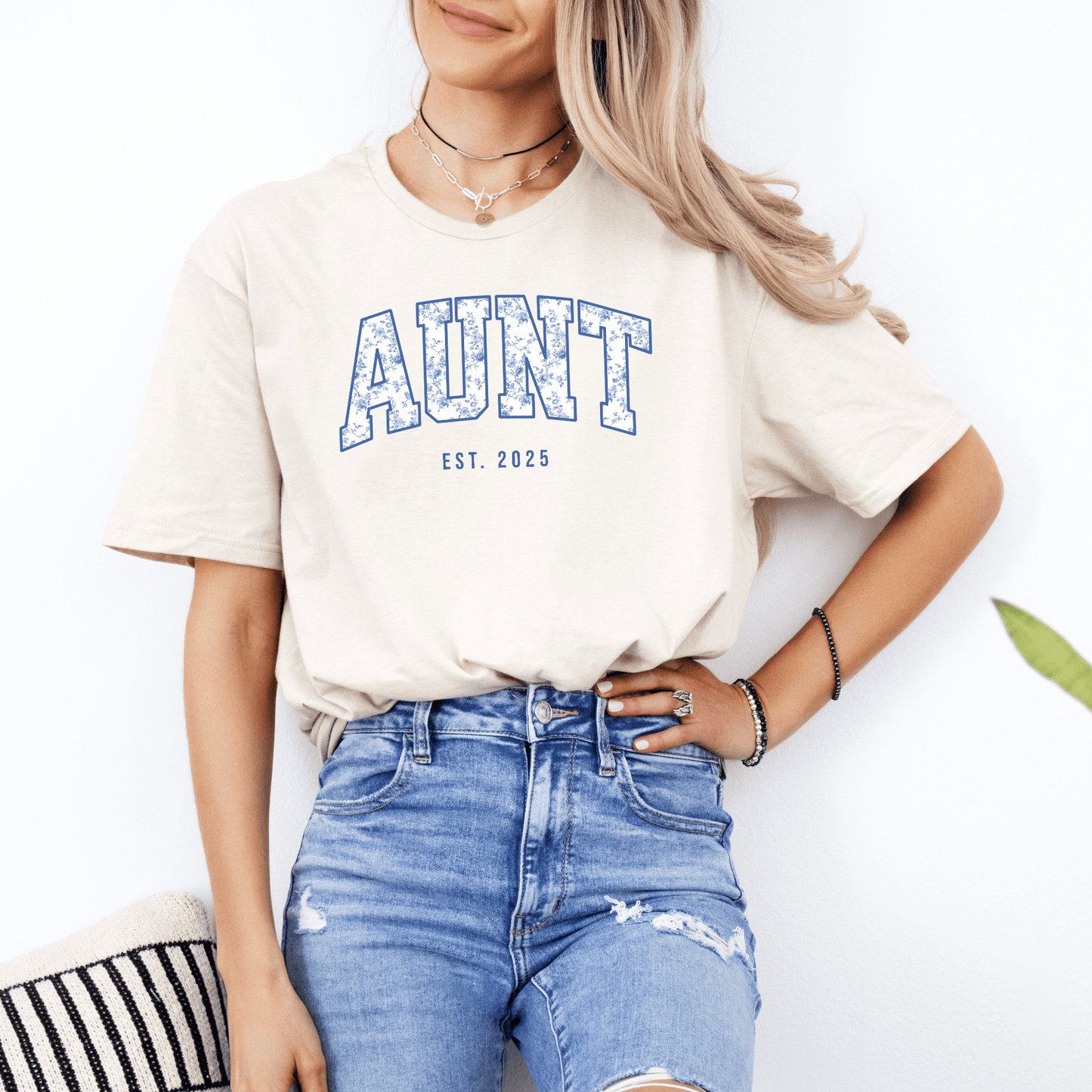 Model wearing Custom Aunt Est. Year Shirt . cream unisex tee with blue collegiate AUNT print and distressed jeans