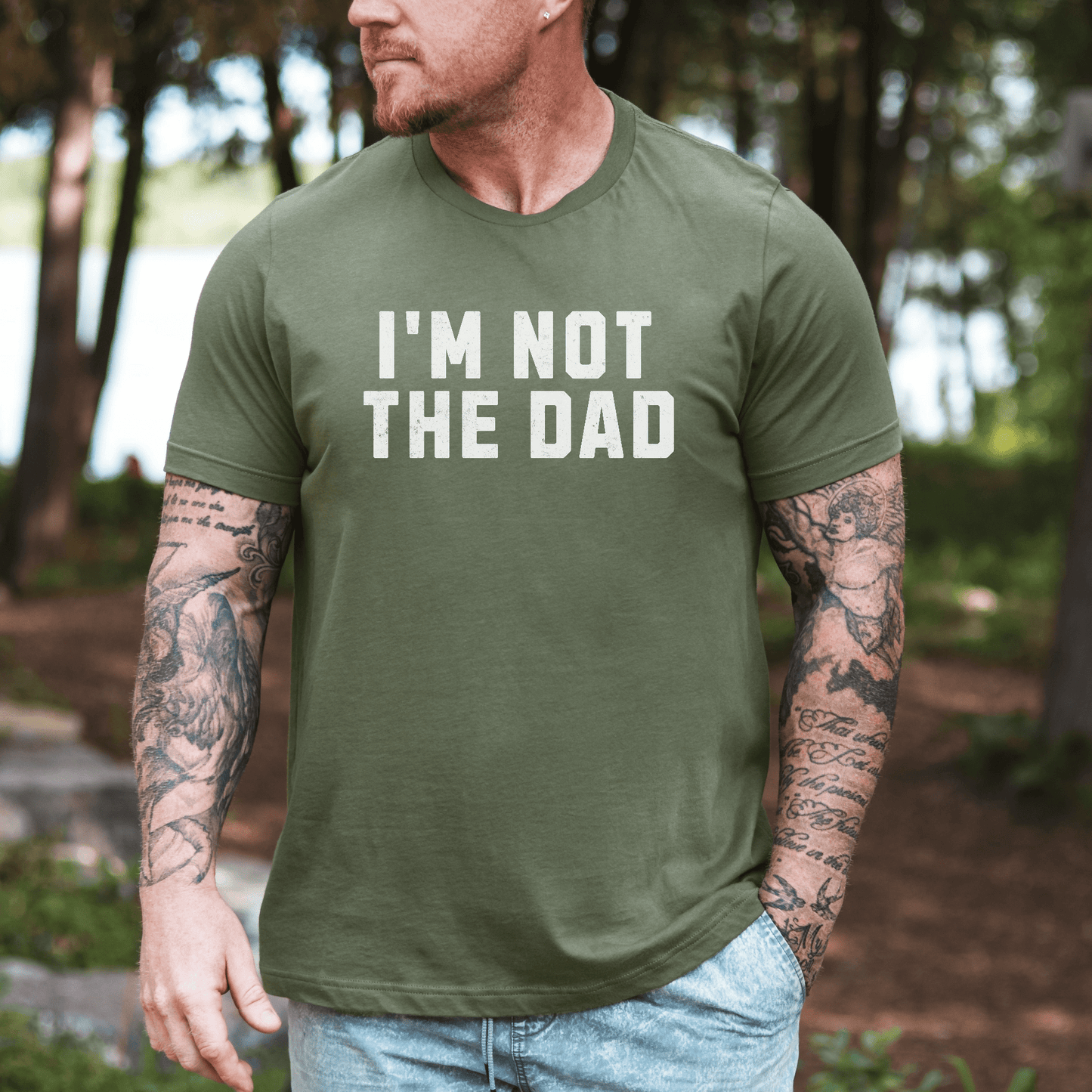 Maddy and George Designs funny I'm not the dad shirt olive green men's tee with bold white text worn by tattooed model outdoors