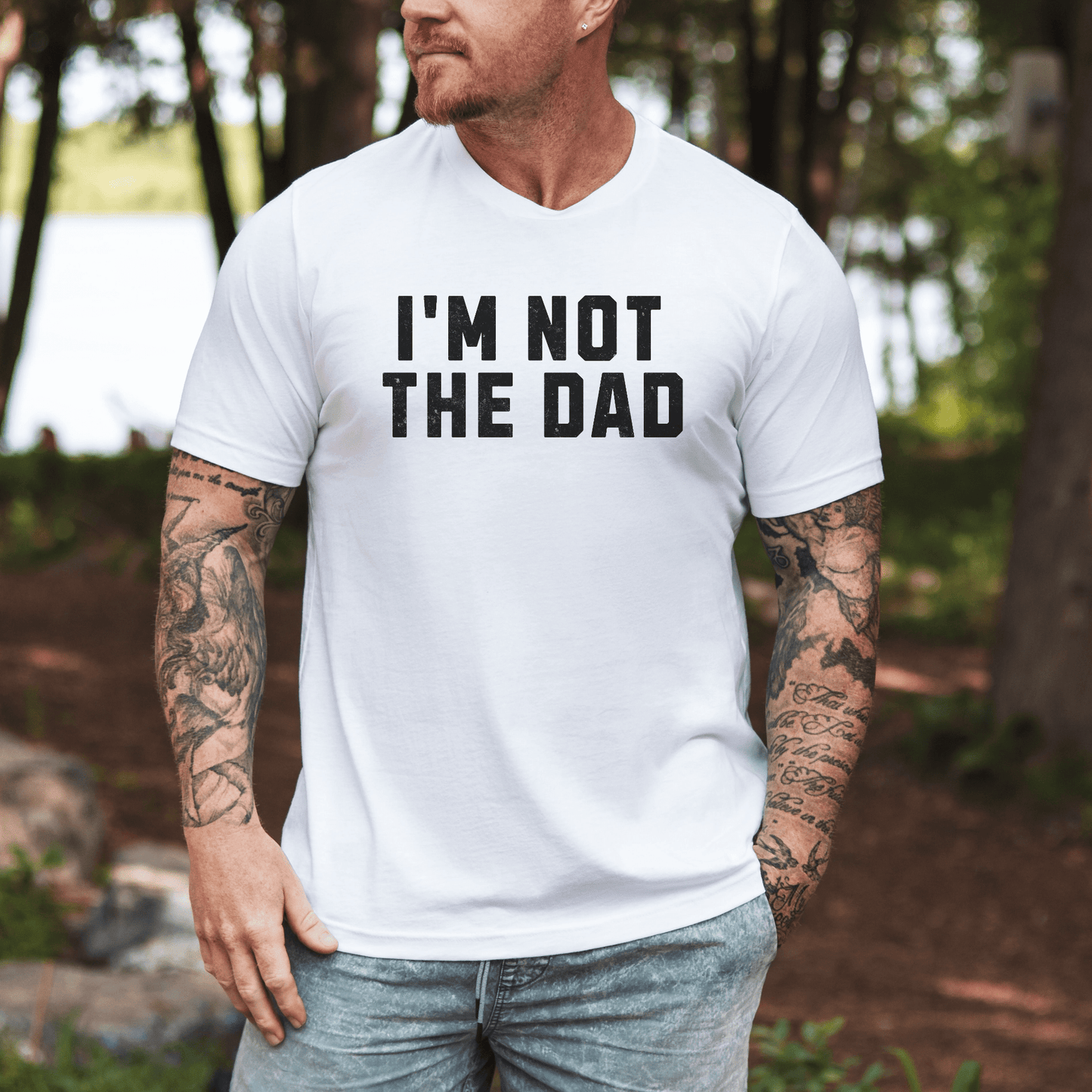 Tattooed man outdoors wearing white tee with bold black text funny I'm not the dad shirt by Maddy and George Designs