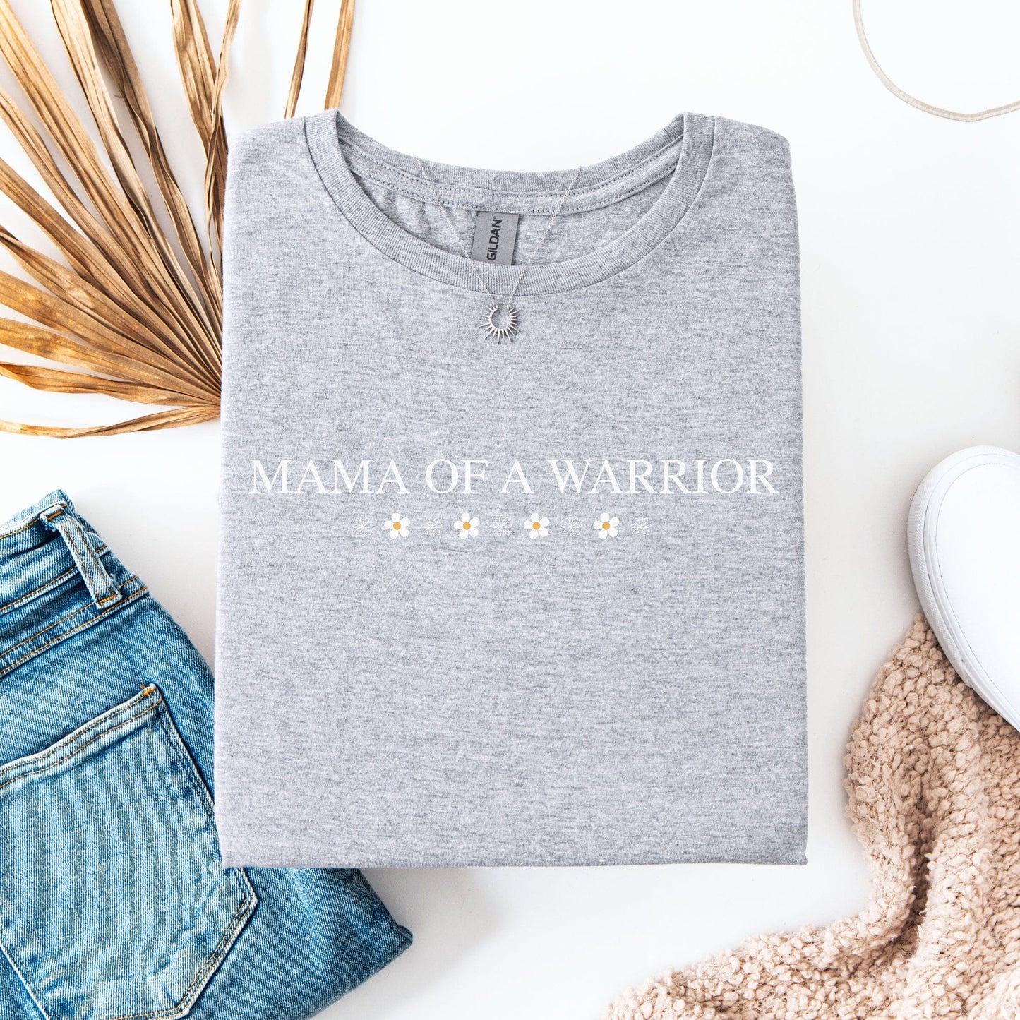 Mama Of A Warrior Shirt gray crewneck with white text and daisy accents flat lay with jeans and sneakers