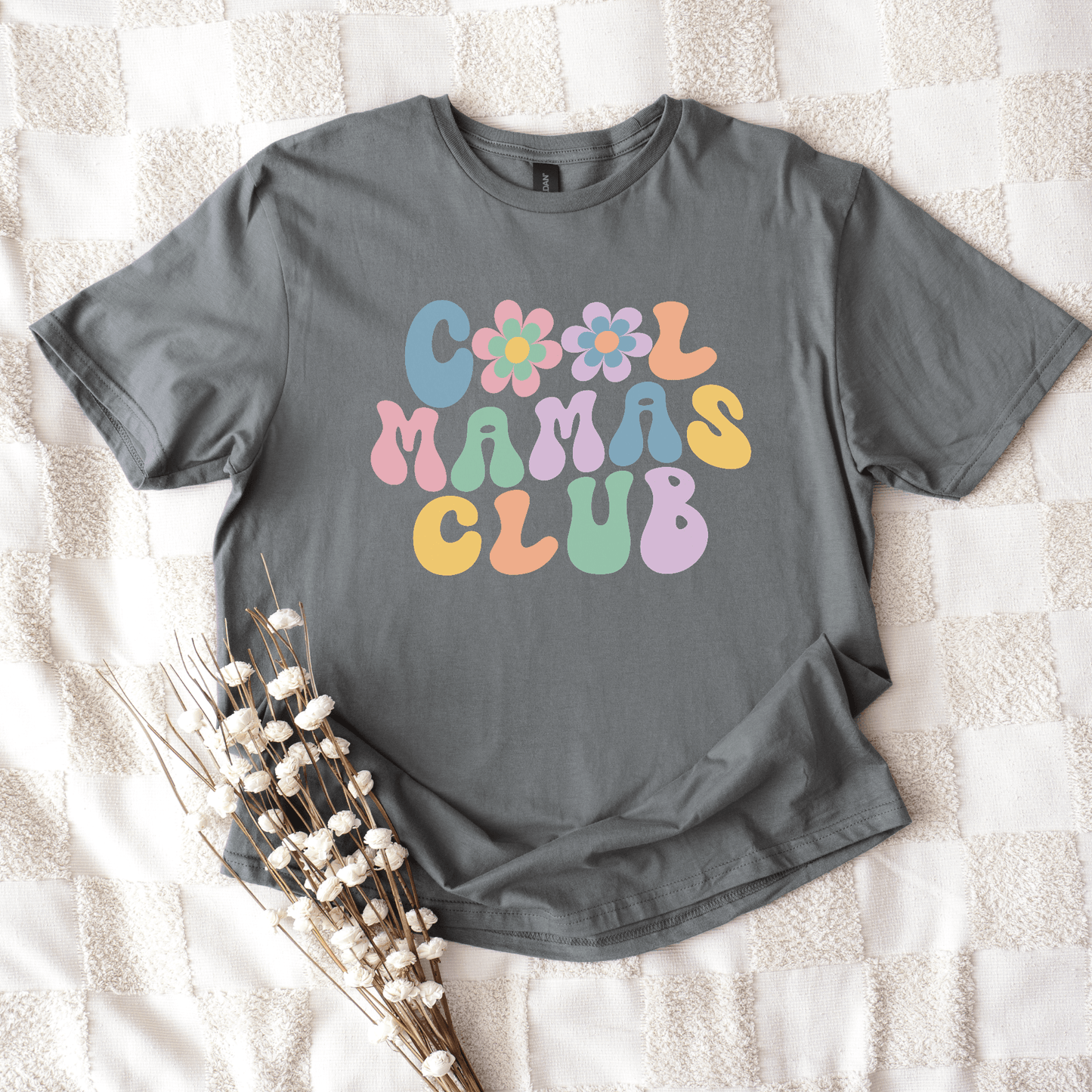 Gray cotton t shirt with retro pastel flower lettering reading Cool Mamas Club Shirt laid on blanket