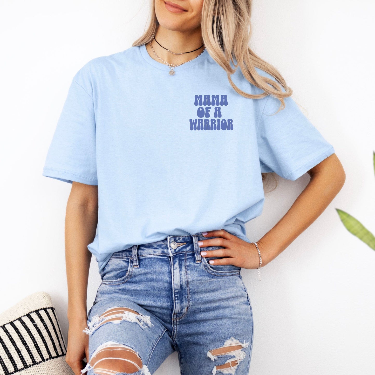 Light blue casual tee with small chest print reading Mama of a Warrior Club Shirt modeled with distressed jeans