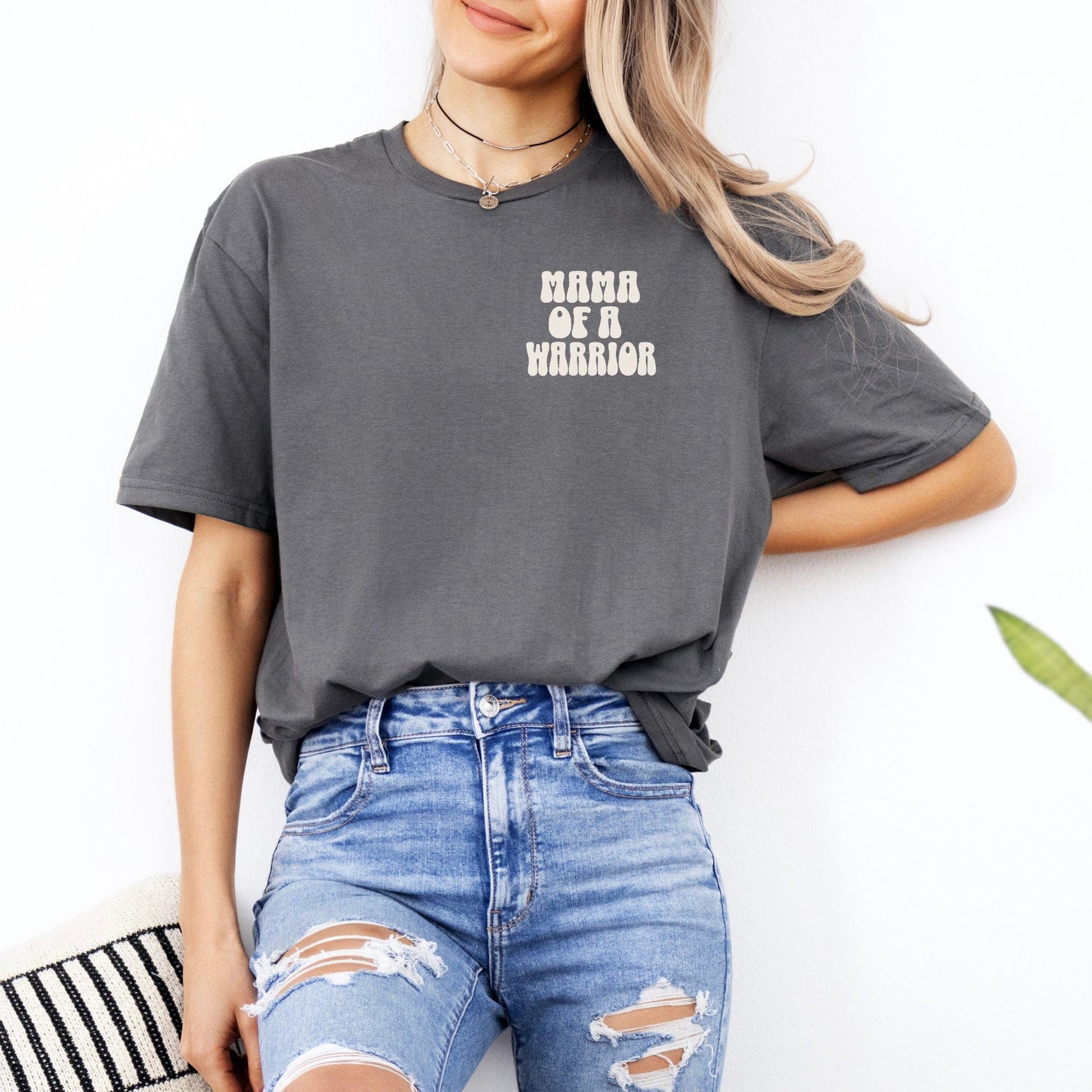 Woman wearing gray Mama of a Warrior Club Shirt tucked into ripped blue jeans casual look