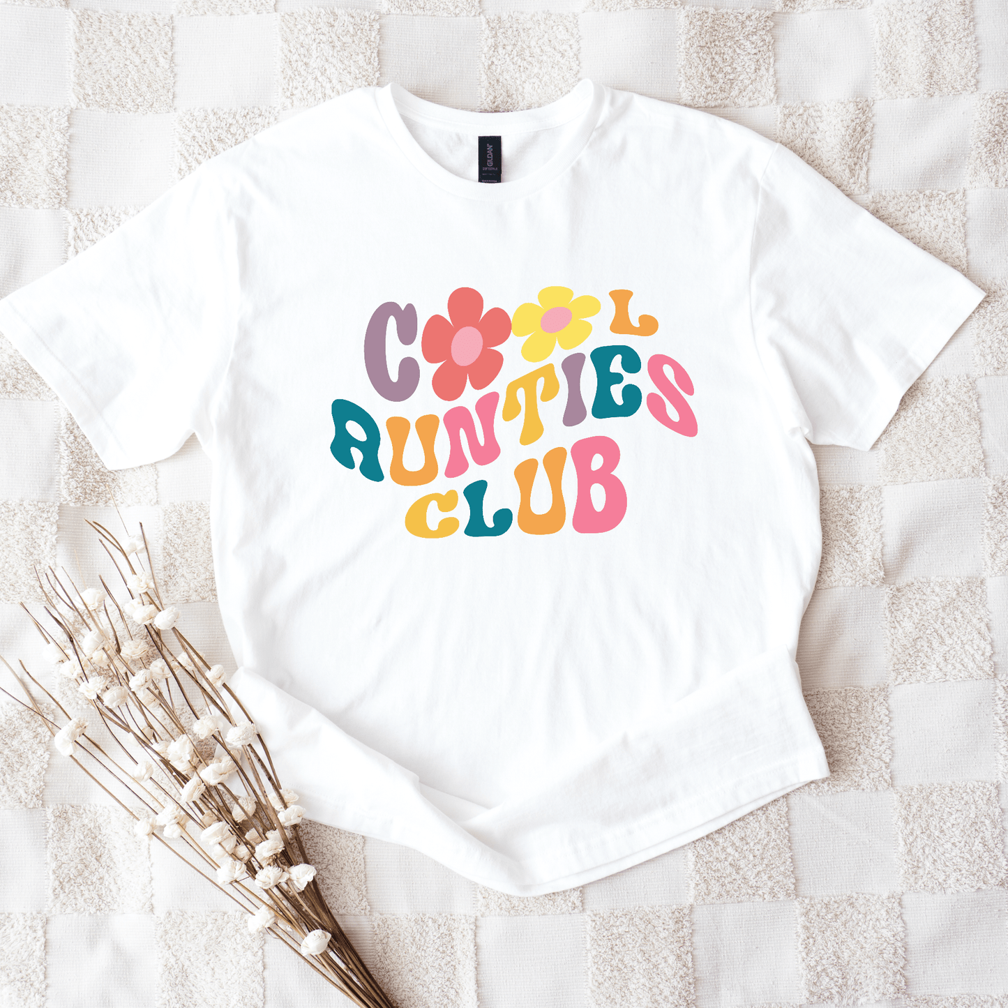 White tee displaying Retro Cool Aunties Club design with colorful 70s style lettering and floral graphics
