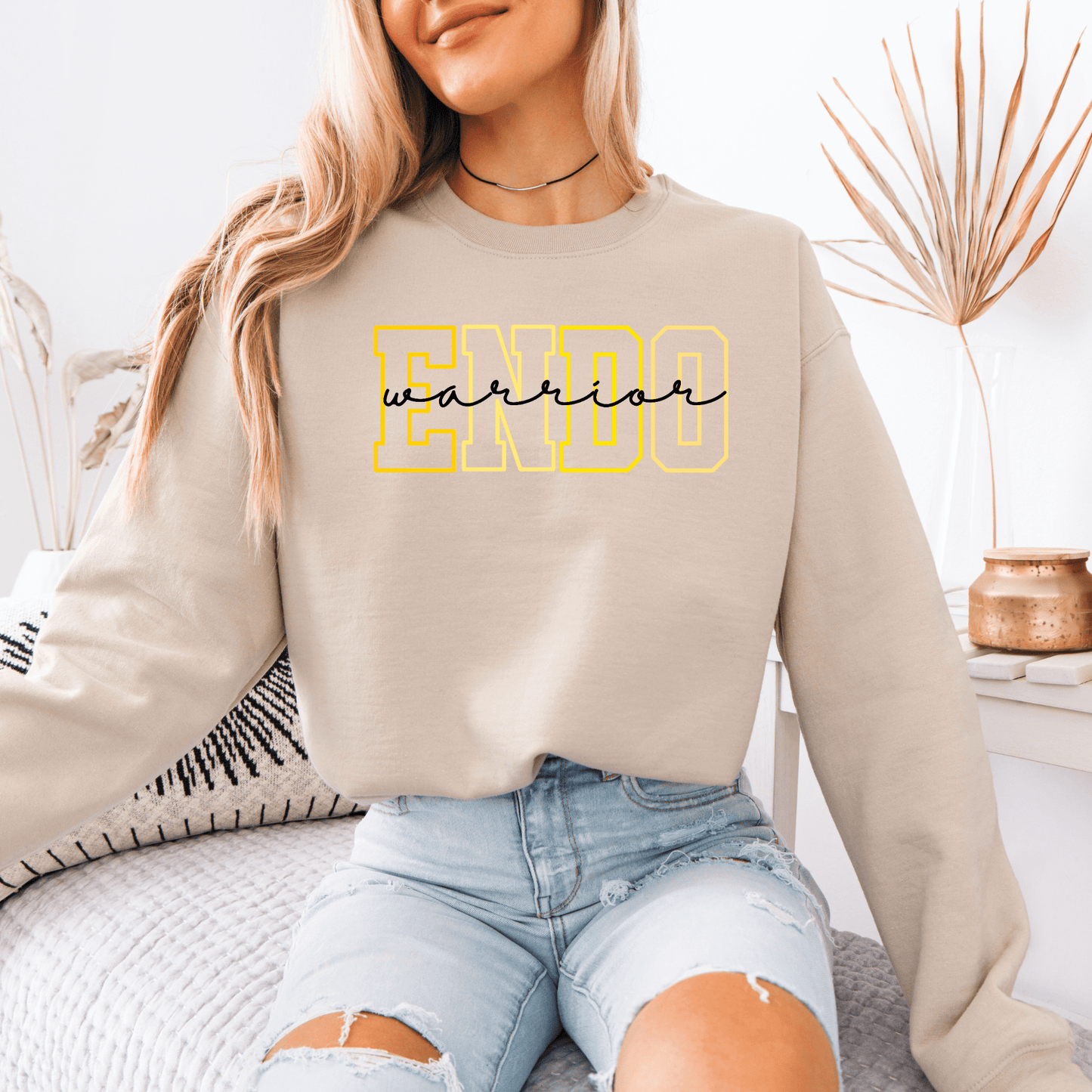 Maddy and George Designs Endometriosis Warrior Sweatshirt beige pullover with yellow outlined ENDO lettering worn by seated woman