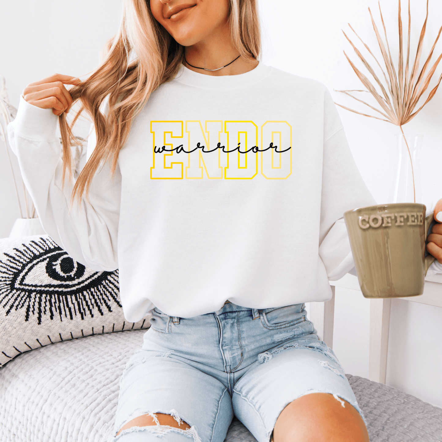 Model wearing white Endometriosis Warrior Sweatshirt . with yellow ENDO letters and black script warrior holding coffee mug