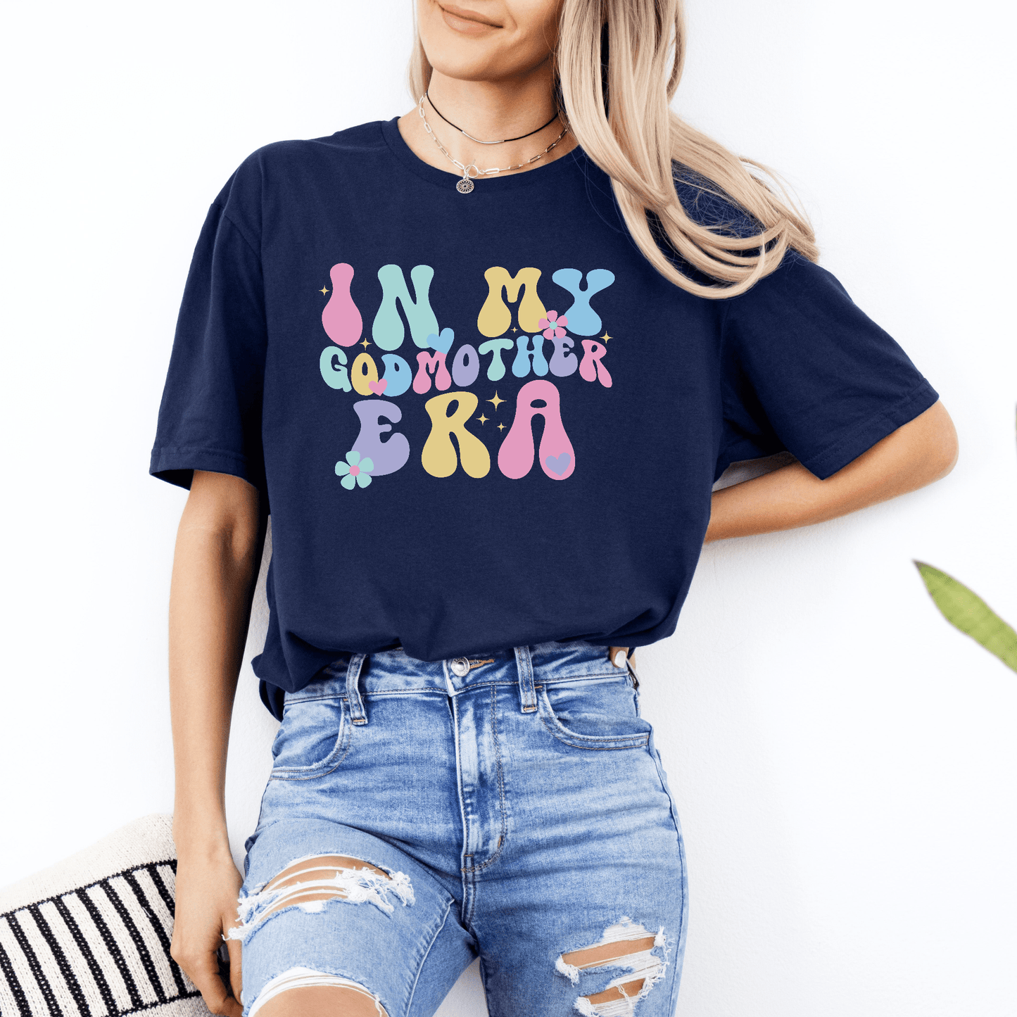 Woman wearing navy Godmother Announcement Shirt with colorful retro In My Godmother Era design tucked into jeans