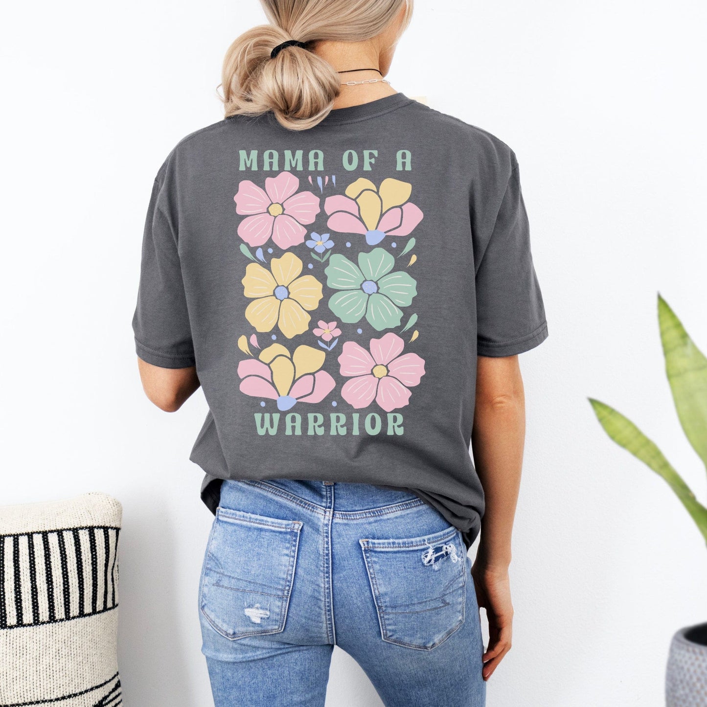 Back view of woman wearing charcoal tee with pastel floral graphic and Mama of a Warrior text Mother of a Warrior Boho Shirt