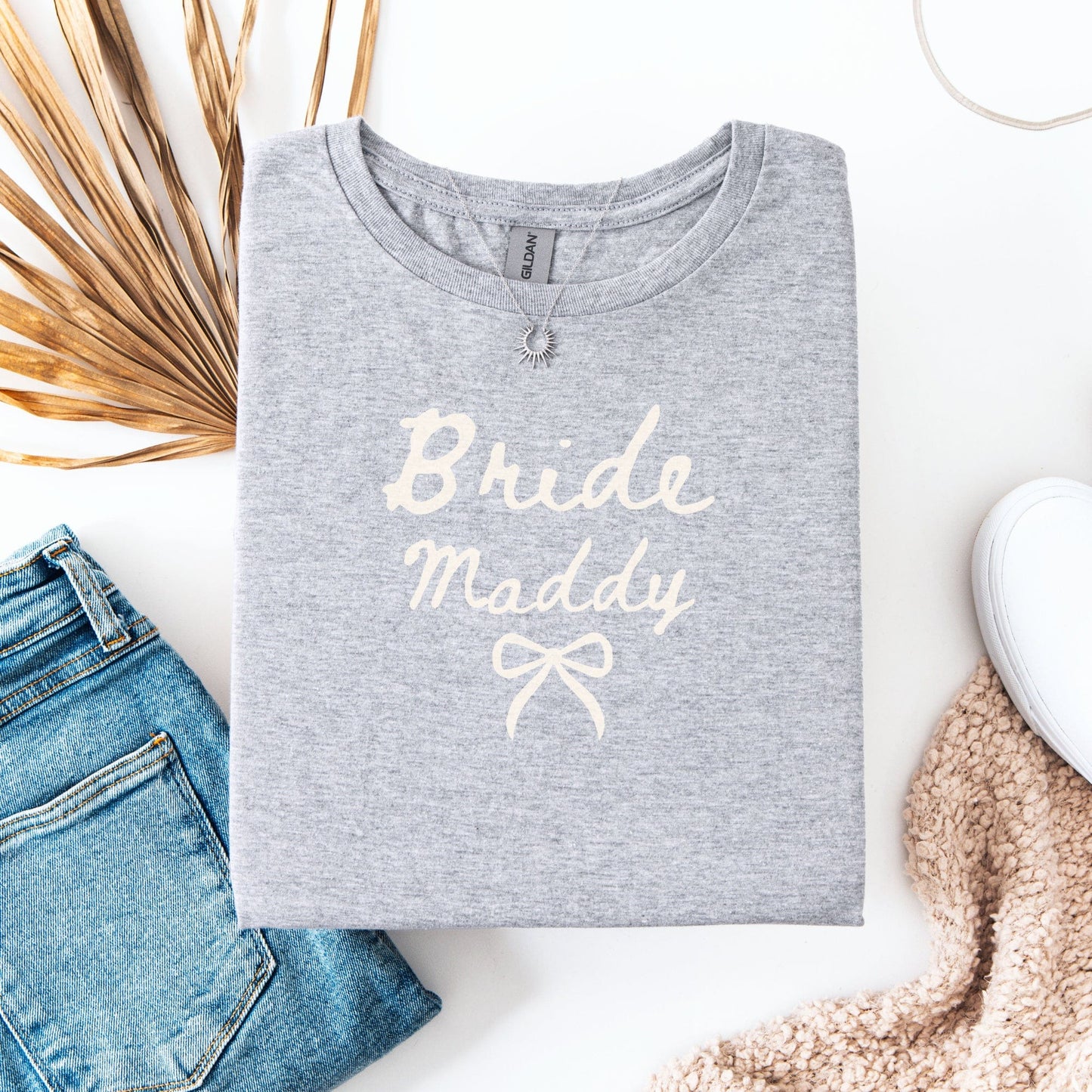Gray folded Custom Bride T-Shirt with name Maddy in script and bow styled with jeans and sneakers