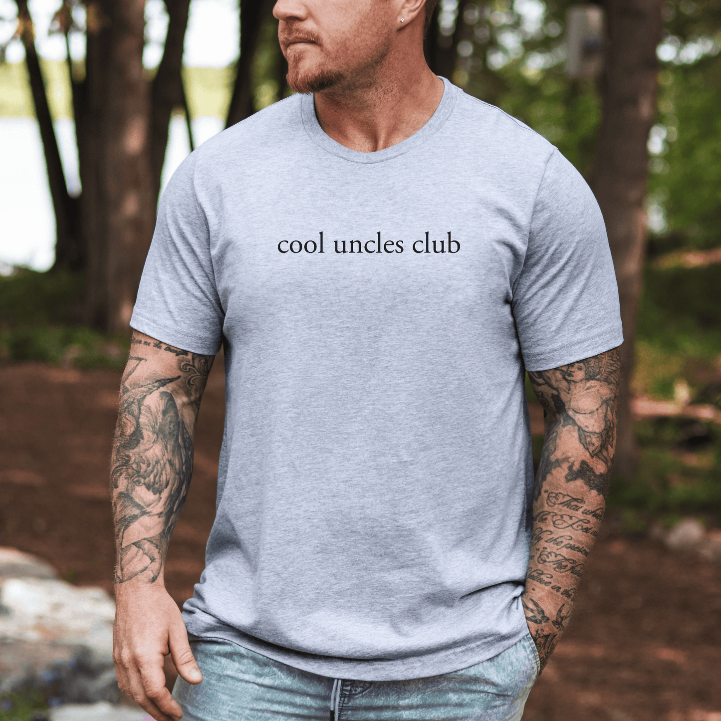 Minimalist Cool Uncles Club Shirt light gray tee with black cool uncles club text worn by tattooed man outdoors