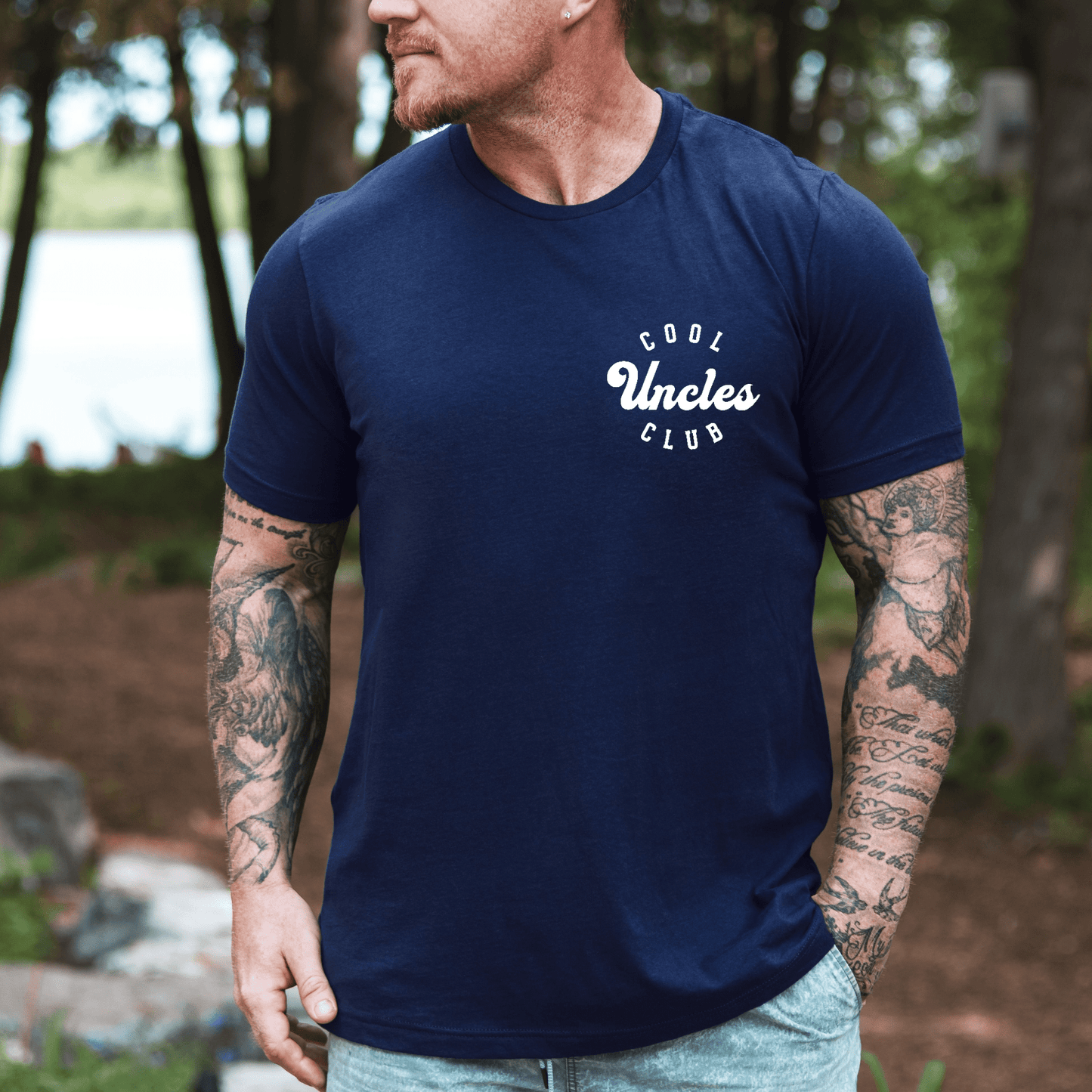 Man wearing navy Cool Uncles Club Shirt with white chest logo casual cotton tee outdoors by lake