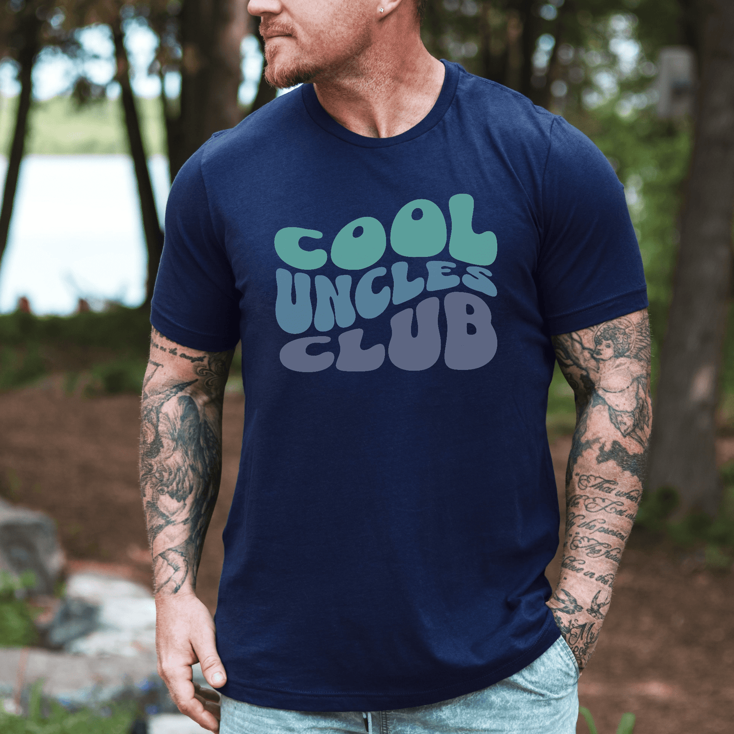 Maddy and George Designs navy tee featuring retro bubble text Cool Uncles Club T-Shirt . worn by tattooed man outdoors