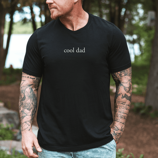 Minimalist Cool Dad Shirt by Maddy and George Designs black tee with small white cool dad text worn outdoors