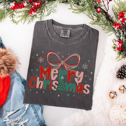 Preppy Merry Christmas Shirt folded charcoal gray tee with red bow and Christmas tree graphic surrounded by holiday decor