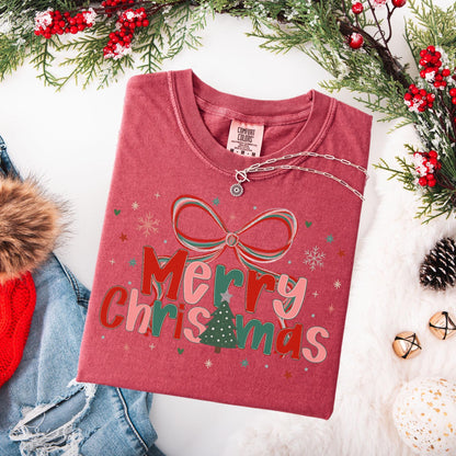 Preppy Merry Christmas Shirt folded red tee with bow and tree graphic styled with denim jacket and holiday greenery