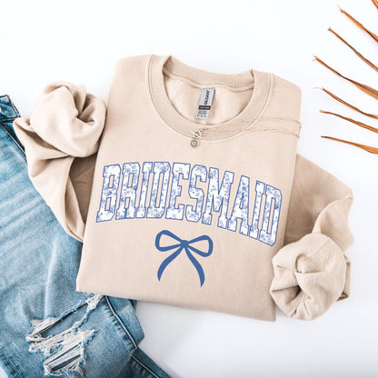 Chinoiserie Bridesmaid Sweatshirt beige folded with blue floral patterned letters and bow beside ripped denim