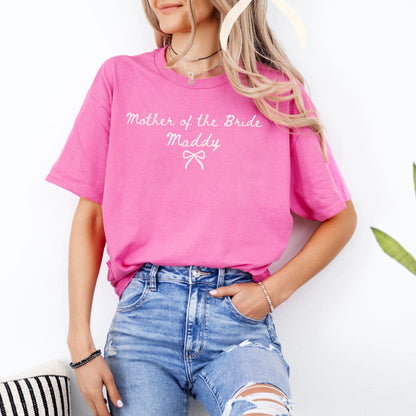 Woman wearing bright pink Custom Mother of the Bride Shirt with white script and bow paired with ripped jeans