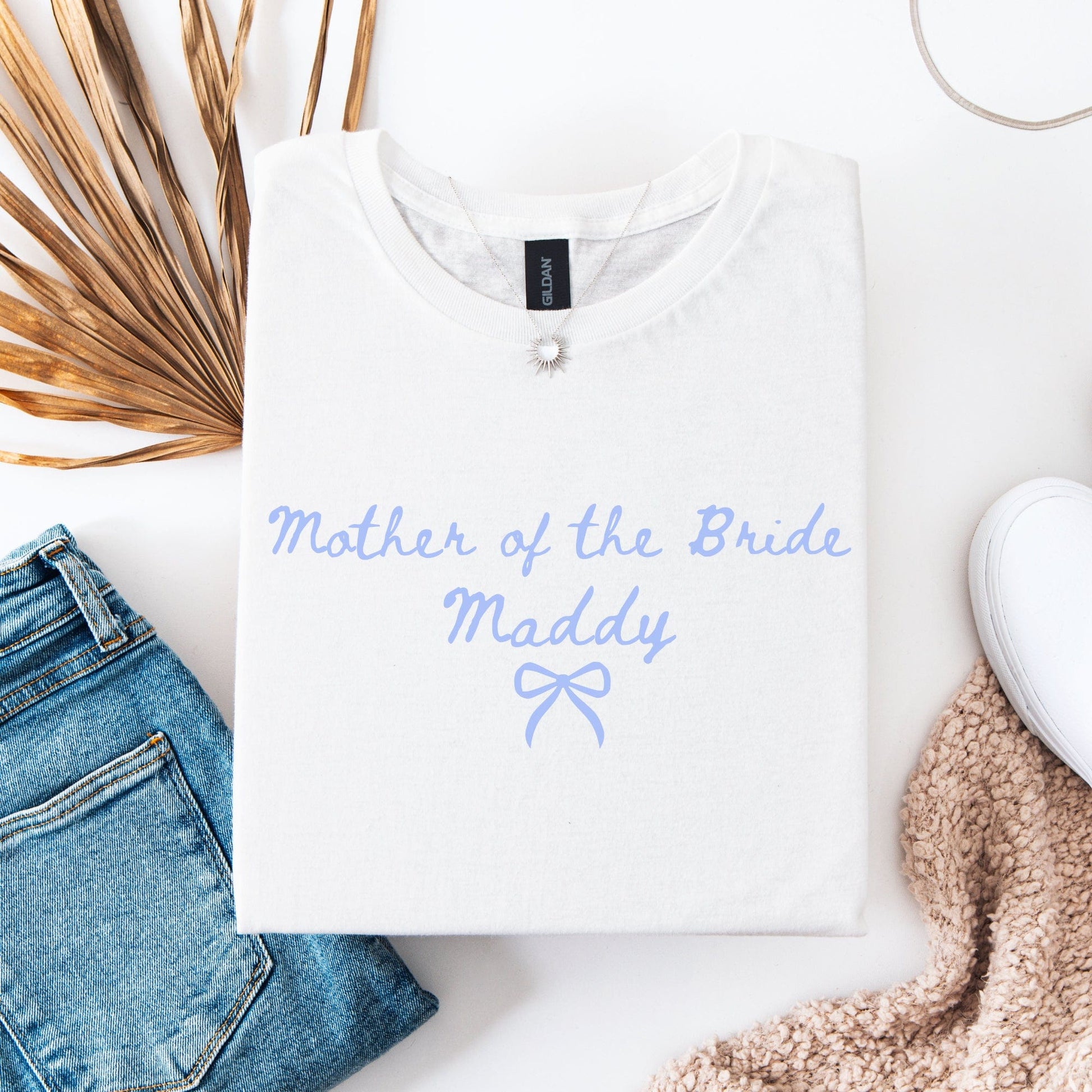 Custom Mother of the Bride Shirt folded white tee with light blue script Maddy and bow beside jeans and sneaker