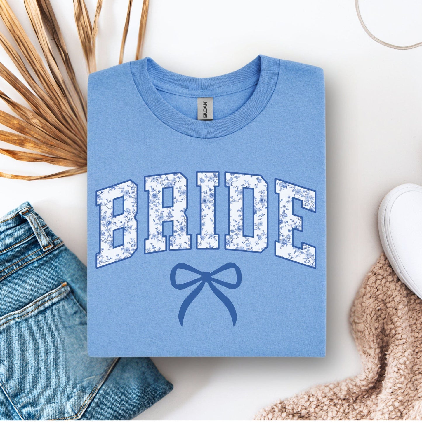 Light blue Chinoiserie Bride T-Shirt folded showing floral varsity BRIDE letters and bow in flatlay