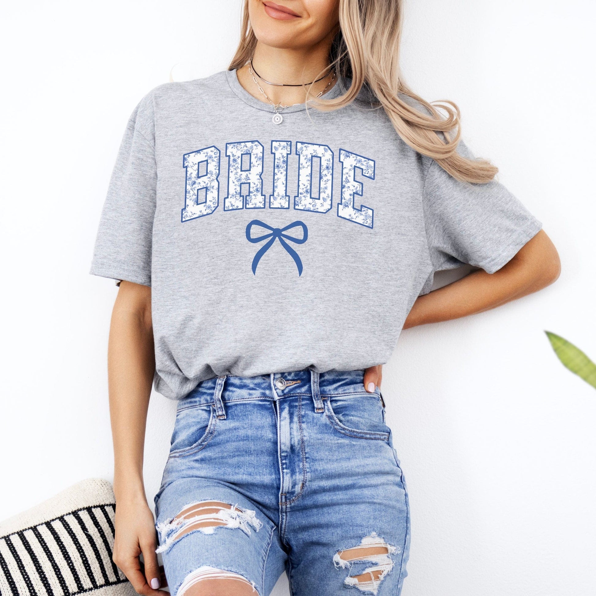 Woman wearing gray Chinoiserie Bride T-Shirt . featuring blue floral BRIDE letters and bow with ripped jeans