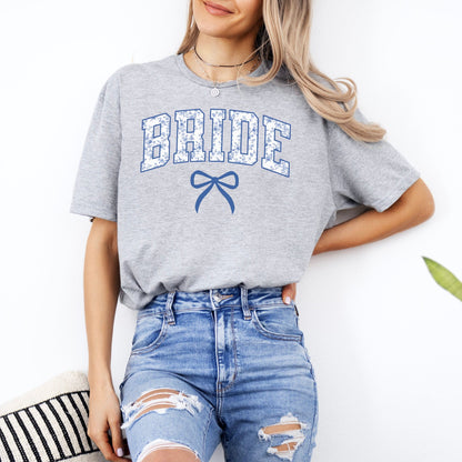 Woman wearing gray Chinoiserie Bride T-Shirt . featuring blue floral BRIDE letters and bow with ripped jeans