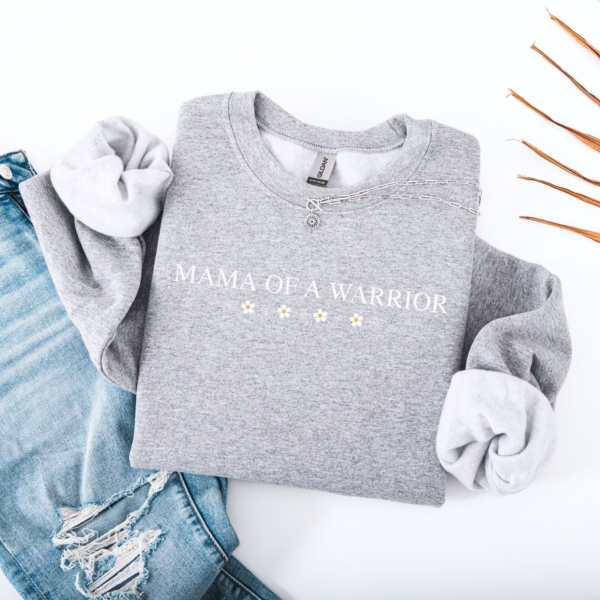 Grey Mama of a Warrior Sweatshirt folded with small daisy print styled with distressed jeans and necklace