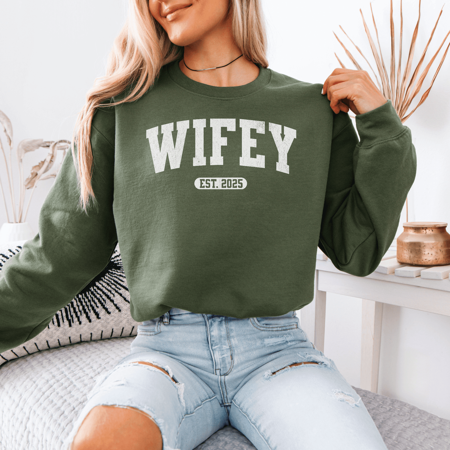 Smiling woman wearing olive green custom wifey sweatshirt with WIFEY EST 2025 print paired with ripped jeans