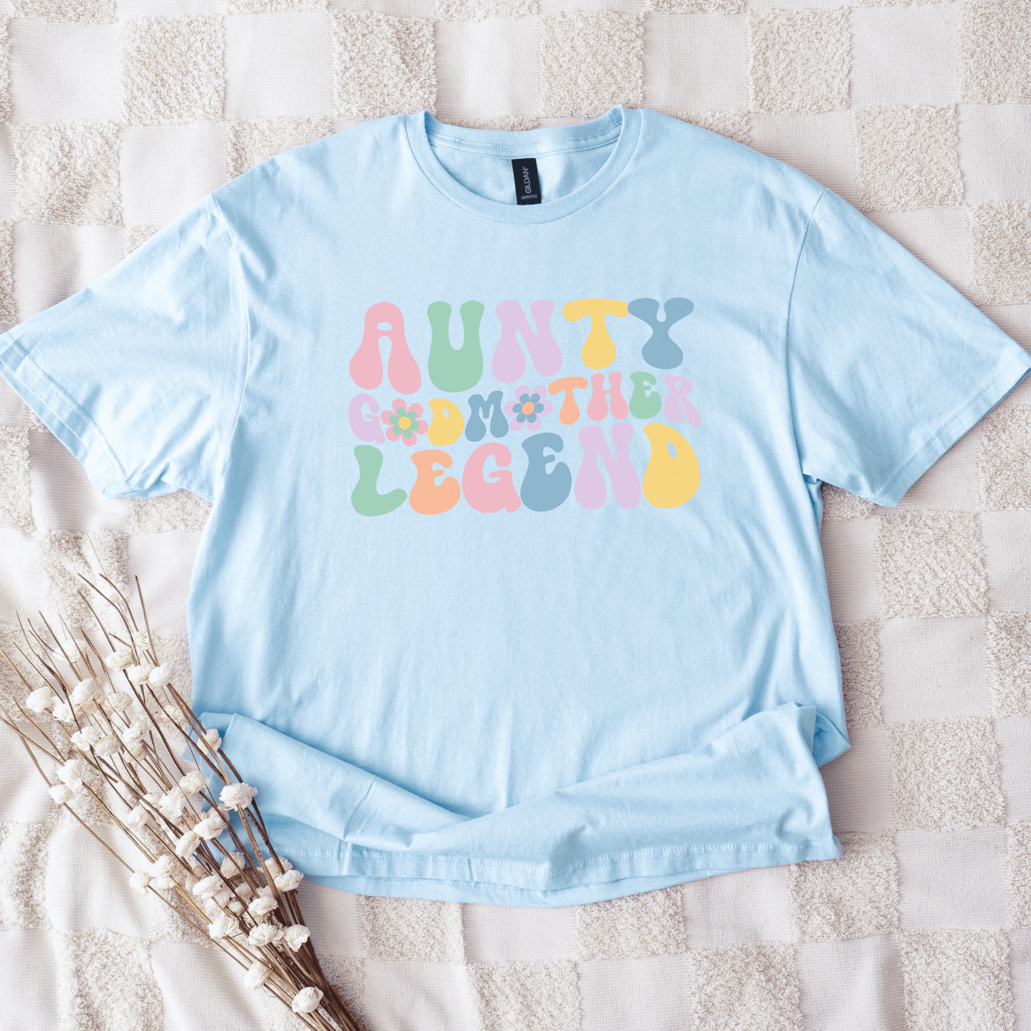 Maddy and George Designs light blue aunty godmother legend shirt with pastel retro bubble letters and floral accents on blanket