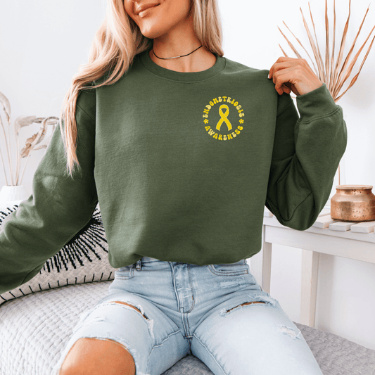 Woman wearing olive green Endometriosis Awareness Sweatshirt with small yellow ribbon logo seated casually in jeans