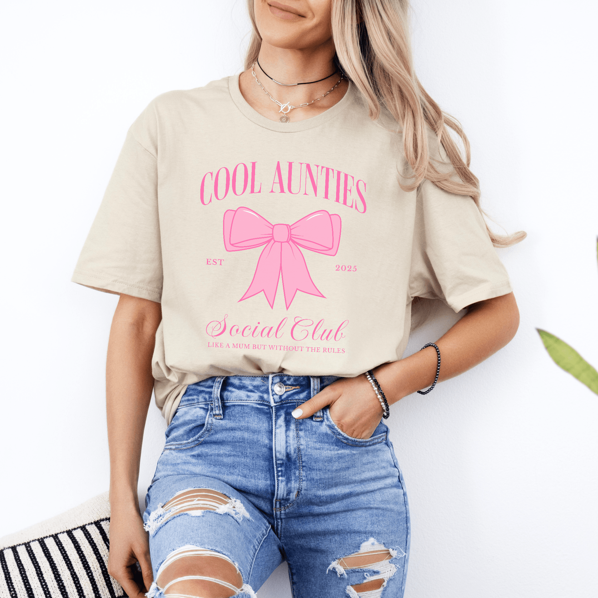 Model wearing Custom Cool Aunties Club Shirt beige tee with pink bow print and casual ripped jeans