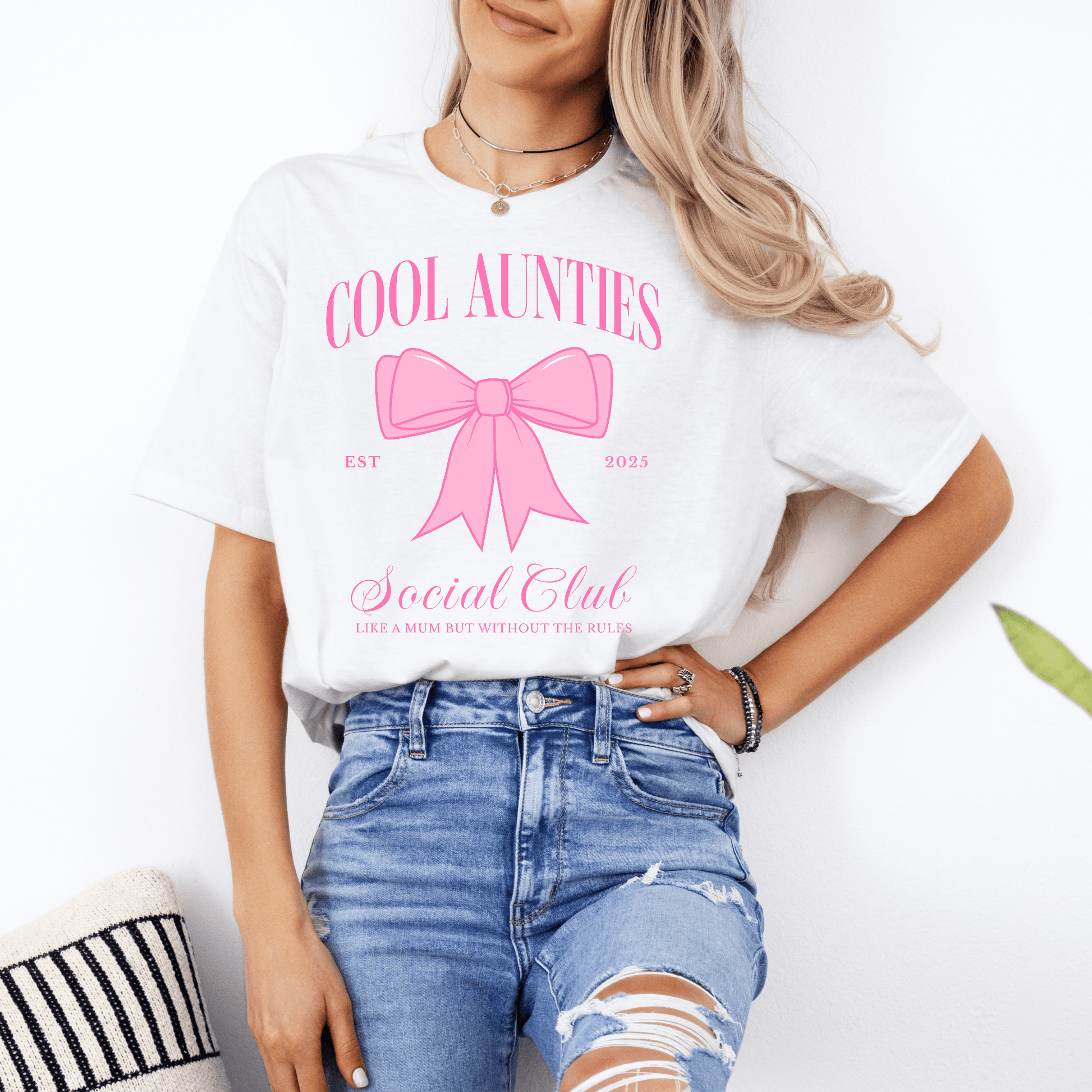 Model wearing Custom Cool Aunties Club Shirt white tee with pink bow graphic and social club print styled with ripped jeans