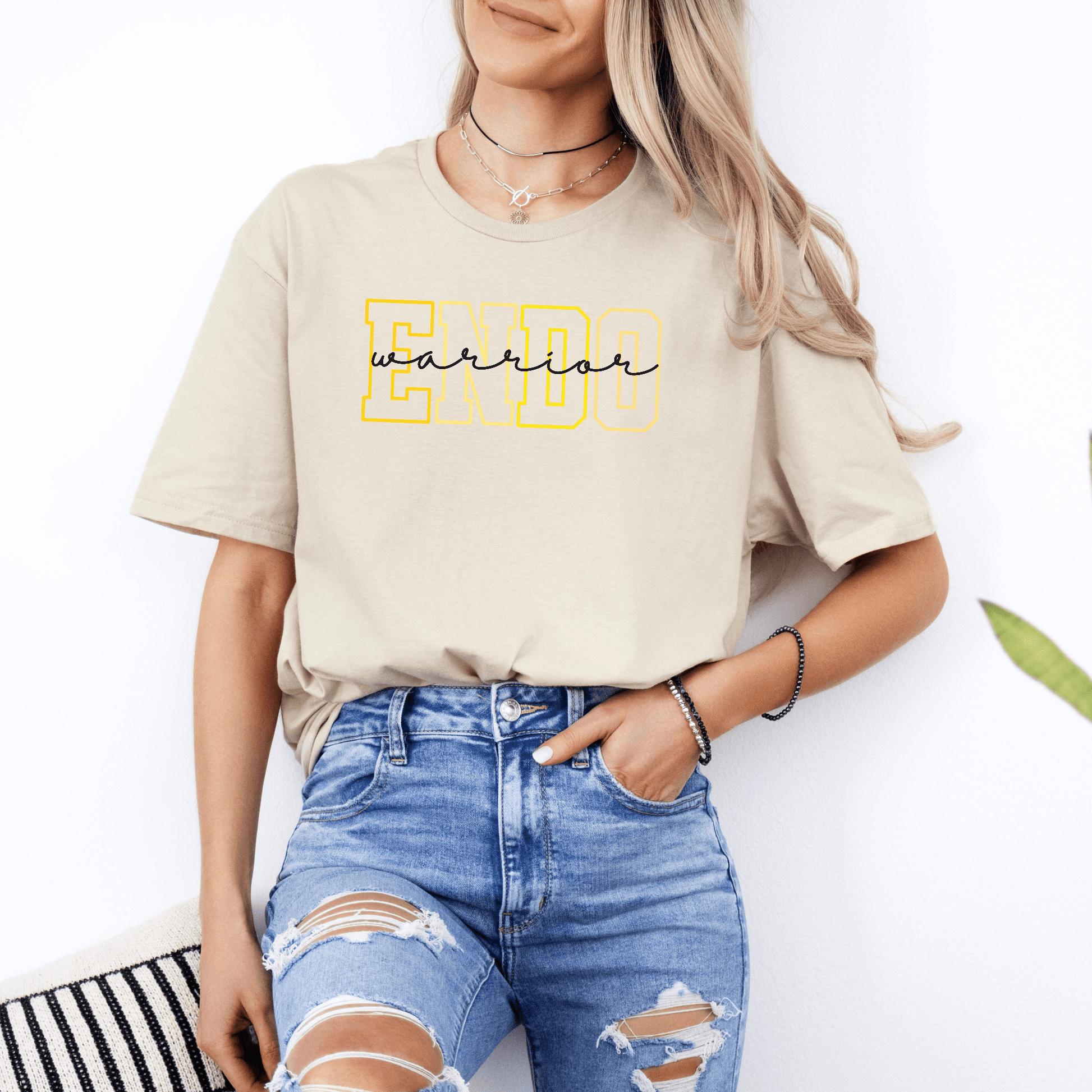 Woman wearing beige Endometriosis Awareness Shirt | Gift For Endo Warrior with yellow ENDO graphic and distressed jeans