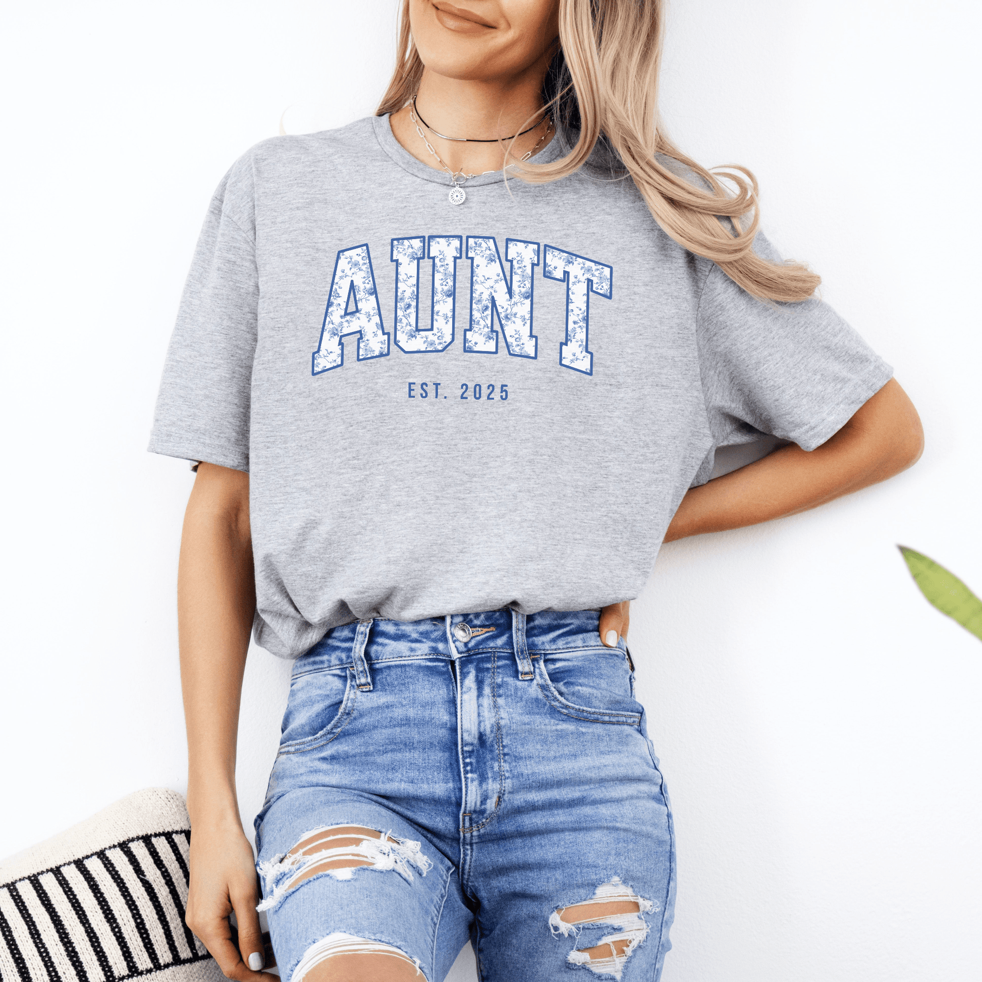 Woman wearing gray Custom Aunt Est. Year Shirt . with blue distressed AUNT print paired with ripped jeans by Maddy and George
