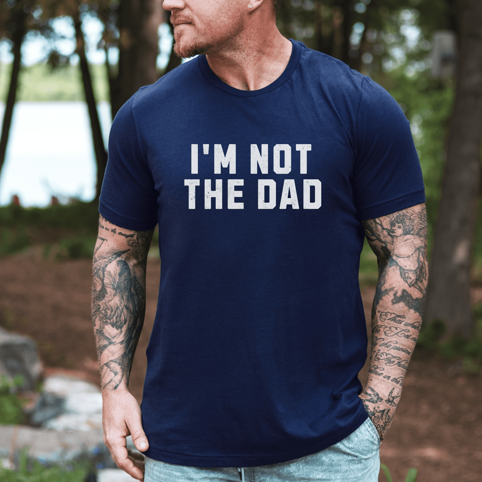 Man with tattoos outdoors wearing navy tee with bold white print reading I'M NOT THE DAD funny I'm not the dad shirt