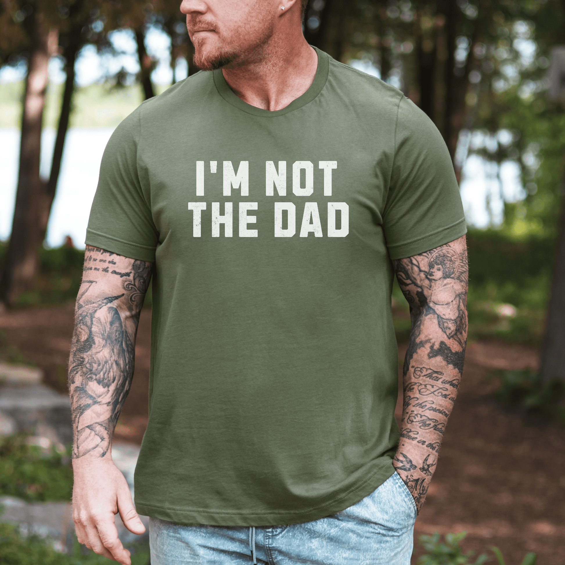 Maddy and George Designs funny I'm not the dad shirt olive green men's tee with bold white text worn by tattooed model outdoors
