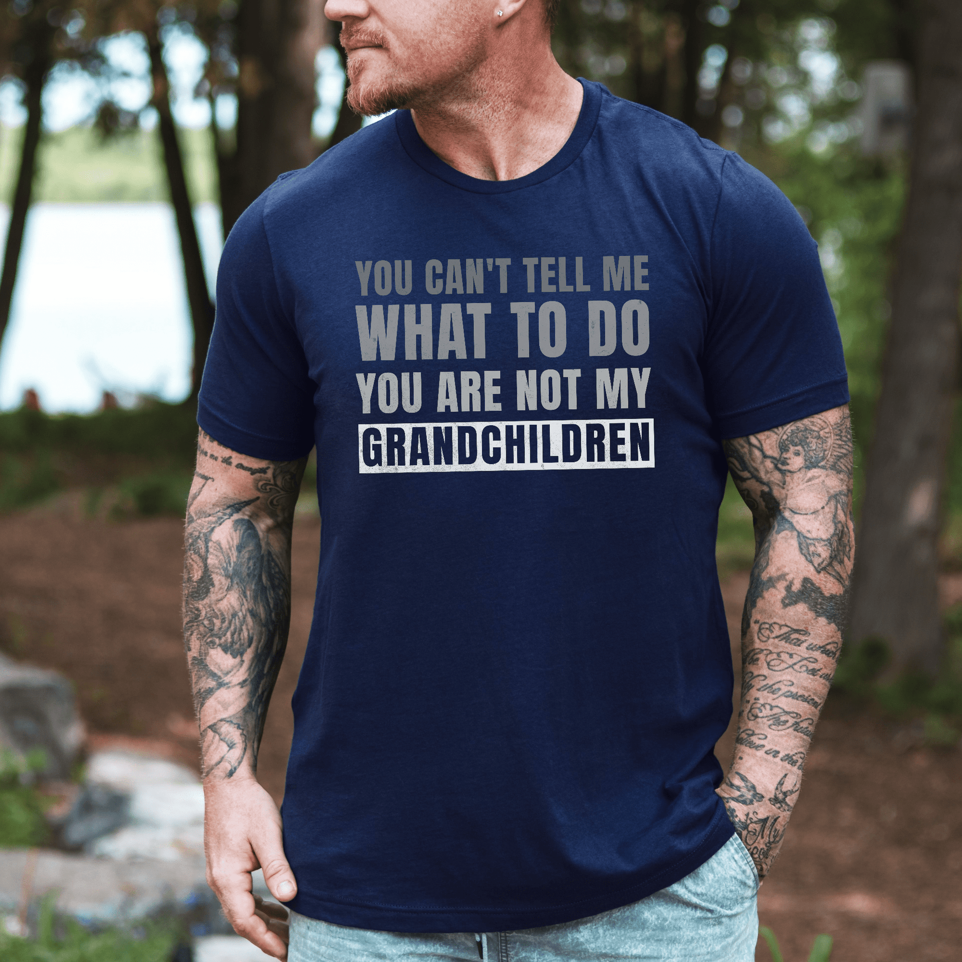 Funny Grandpa T-Shirt navy crewneck with bold humorous grandchildren slogan worn by tattooed man outdoors